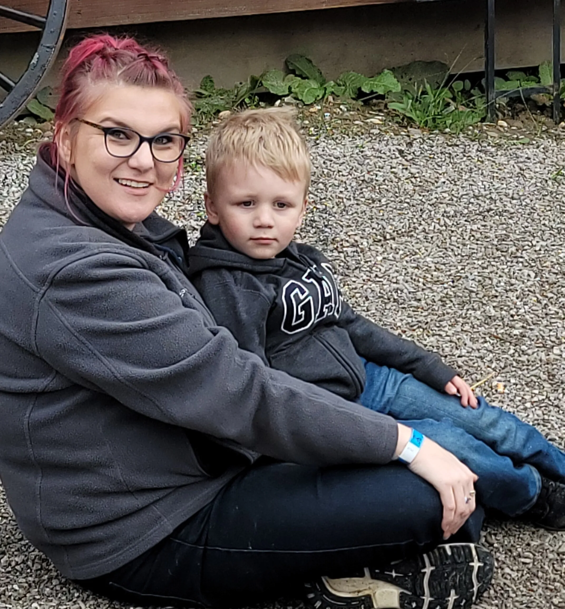 Brittany sitting on the gravel outside with her son on her lap, both in grey hoodies