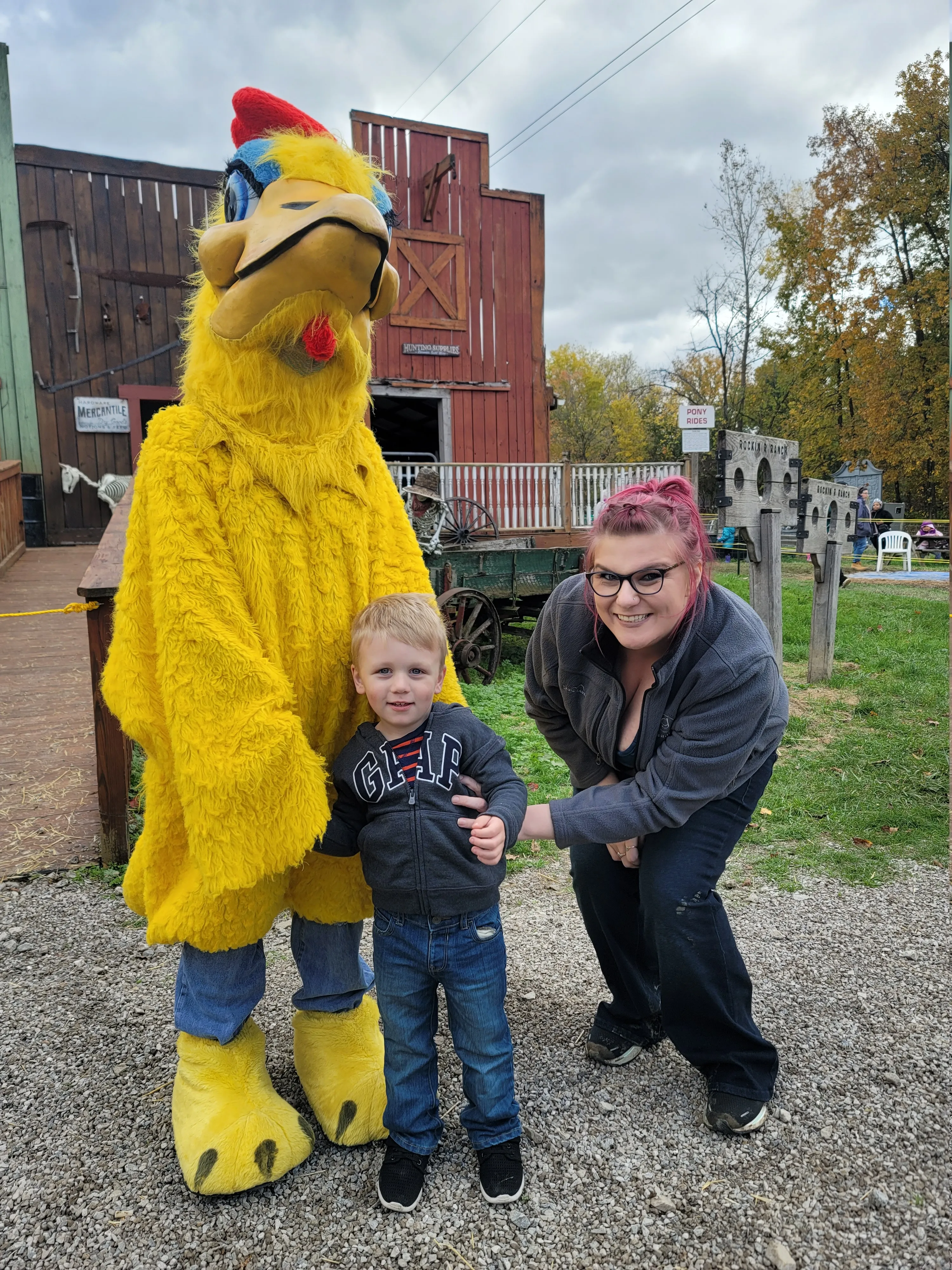 Brittany and her son at a fall farm event, standing next to someone in a giant yellow chicken costume